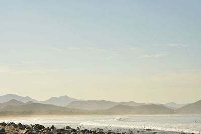 Surfer rides his surf board on white wave pacific coast of baja, mexico with hills and mountain 