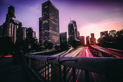 Illuminated modern buildings and light trails on road in city at dusk