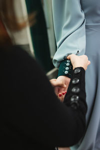 Female tailor attaching buttons with pins on sleeve of dress on model arm during work in professional workshop