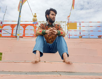 Young man looking away while sitting against sky