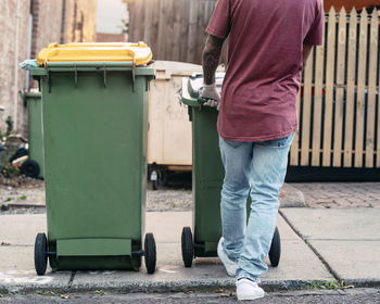 Low section of man with garbage bin standing on street