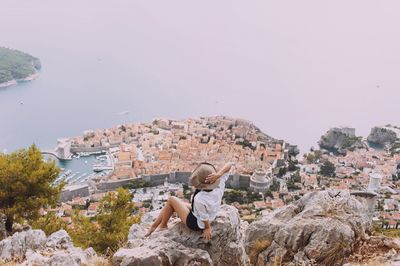High angle view of woman sitting on rock against old town by sea
