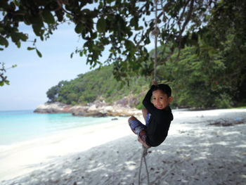 Portrait of boy hanging on rope at beach