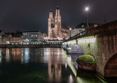 Illuminated buildings by river against sky at night