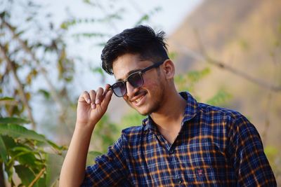 Low angle view of smiling young man wearing sunglasses while standing outdoors