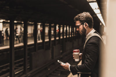 Young businessman waiting at metro station platform, using smart phone