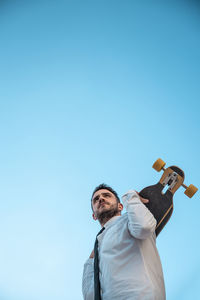 Man with skateboard standing against clear blue sky