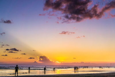 Silhouette people on beach against sky during sunset