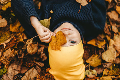 Portrait of a boy a child in a yellow hat holding an autumn leaf and lying in the fall park outdoors