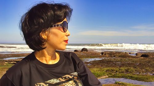 Beautiful young woman wearing sunglasses on beach against sky