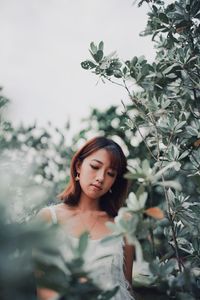 Beautiful young woman looking away while standing by plants