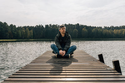 A man enjoys the view while exploring nature while sitting cross-legged on a wooden pier in autumn