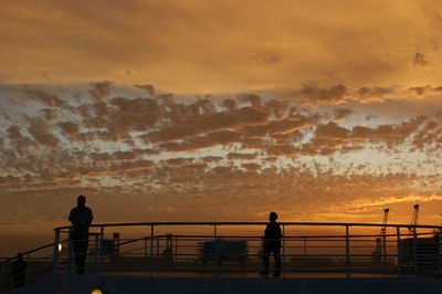 Silhouette of people on railing at sunset