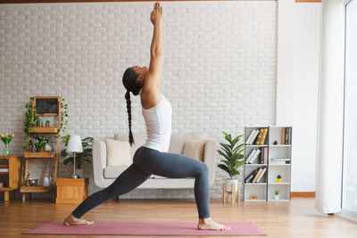 Full length of woman with arms raised on floor at home