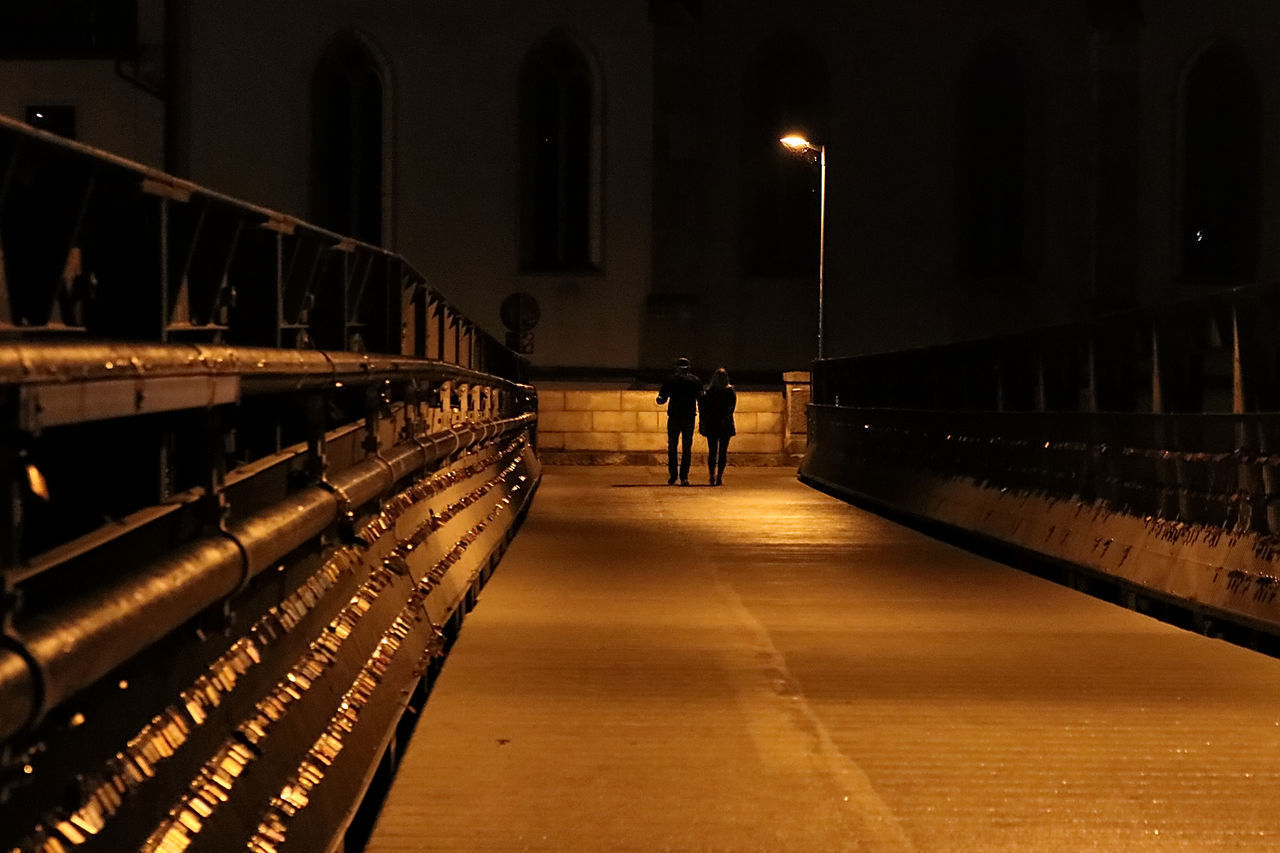 PEOPLE WALKING ON ILLUMINATED BRIDGE AT NIGHT