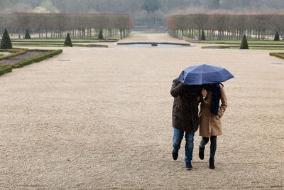 Couple holding umbrella while walking in park during rainy season