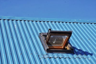 Low angle view of open window on blue metallic roof against clear sky