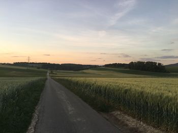 Road amidst field against sky during sunset