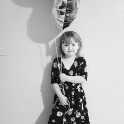 Portrait of girl holding balloon while standing by wall at home