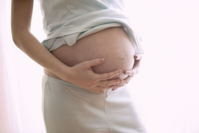 Midsection of pregnant woman with hands against white background