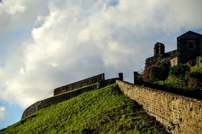 Low angle view of fortified wall on hill against cloudy sky