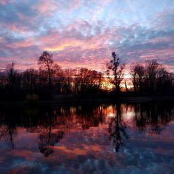 Reflection of silhouette trees in lake against sky during sunset