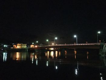 Illuminated city by river against sky at night