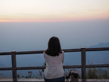 Rear view of woman looking at railing against sky