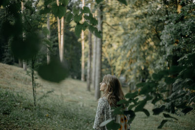 Rear view of woman standing by plants in forest