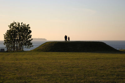 People standing on field against sky during sunset