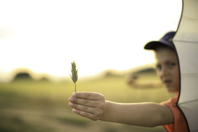 Close-up of hand holding flower against sky