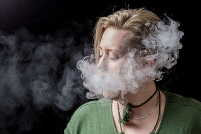 Close-up of woman smoking against black background