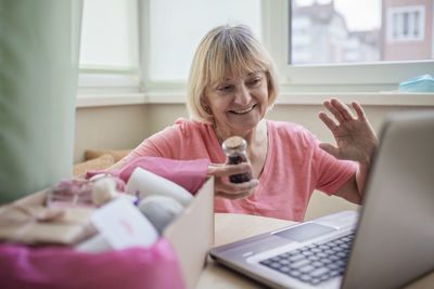 Senior woman holding gift while using laptop at home