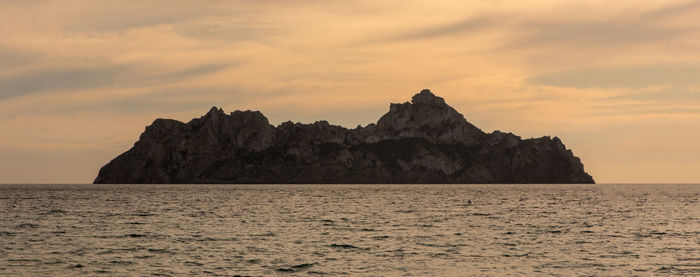 Rock formation in sea against sky during sunset