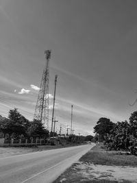 Electricity pylon on road amidst trees against sky