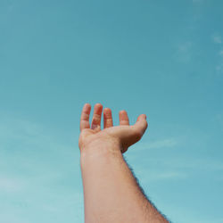 Low angle view of hand against blue sky