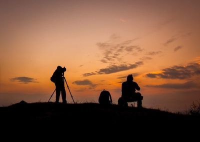 Silhouette man photographing on orange sunset sky