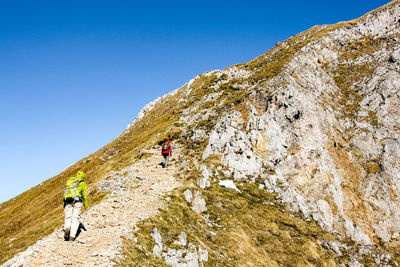 People on rock by mountains against clear blue sky