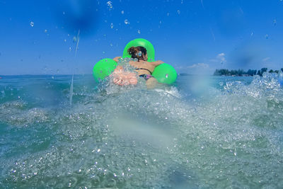 Woman with inflatable swimming in sea against blue sky
