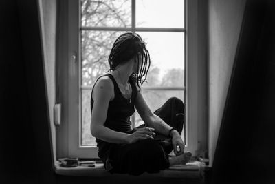 Thoughtful young woman sitting on window sill at home