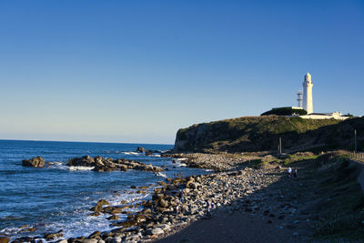 Lighthouse on beach by sea against clear sky