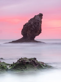 Rock formation on beach against sky during sunset