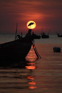 Silhouette boat moored in sea against orange sky