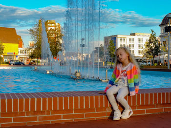 Full length of boy sitting on swimming pool against sky