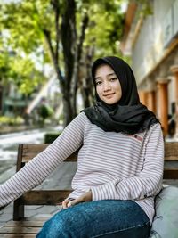 Portrait of smiling young woman sitting on bench in city