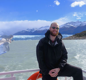 Portrait of smiling man in boat on sea against mountain during winter