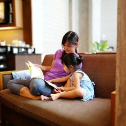 Mother and daughter sitting with spoon on sofa at home