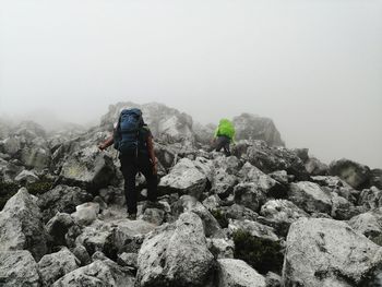 Rear view of person on rock against sky during winter