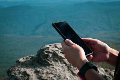 Midsection of person using mobile phone on rock