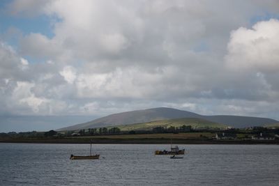 Boats in river against cloudy sky